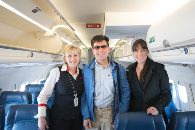 A young man stands onboard a Douglas aircraft between two smiling American women in Delta Airlines uniform